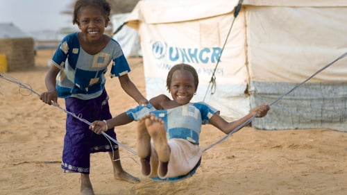 Två flickor som gungar utanför UNHCR-tält.