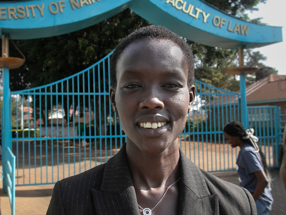 En kvinna står framför ingången till ett universitet. Hon ler mot kameran.