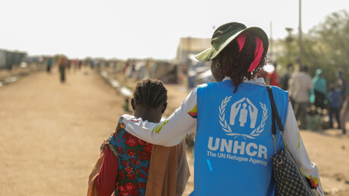 UNHCR-medarbetare och ett barn går på en grusväg.