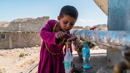 En pojke i Afghanistan hämtar vatten ur en kran.