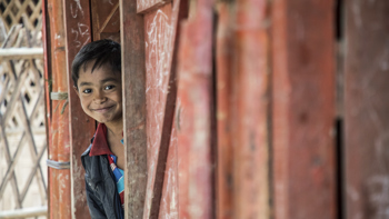 En pojke tittar ut bakom ett skynke.