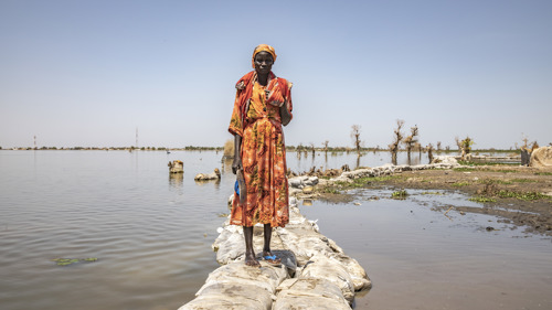 En kvinna står på en väg. Runt henne är markerna översvämmade.