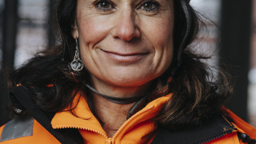 En kvinna klädd i byggkläder tittar in i kameran.