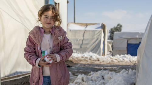 En flicka har kramat en snöboll. Hon tittar mot kameran.