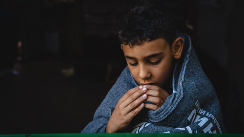 En syrisk pojke sitter insvept i en varm filt.