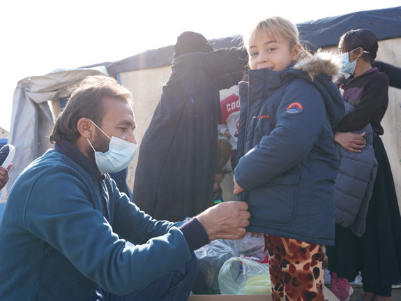 En hjälparbetare hjälper en flicka att ta på sig en jacka.