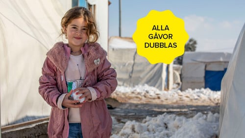 En flicka har kramat en snöboll. Hon tittar mot kameran.