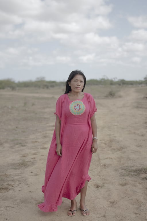 En kvinna i rosa klänning står vid en ödslig väg. Hon tittar in i kameran och ser allvarlig ut.