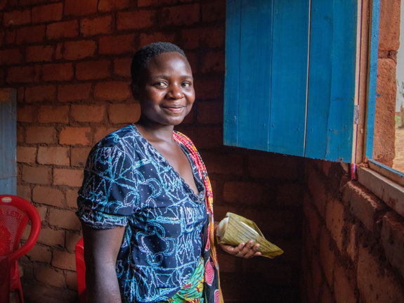 En kvinna sitter på ett golv. Hon tittar in i kameran och ler.