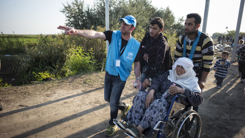UNHCR-personal vägleder människor, en i rullstol, att hitta en säker plats.