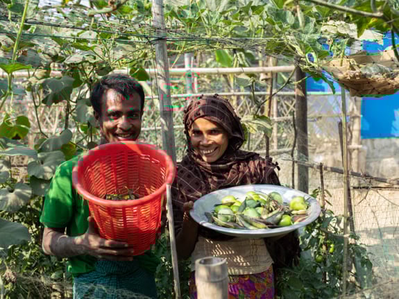 En man och en kvinna visar upp sina odlade grönsaker för fotografen.