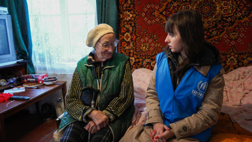 En äldre kvinna och en UNHCR-medarbetare sitter intill varandra.