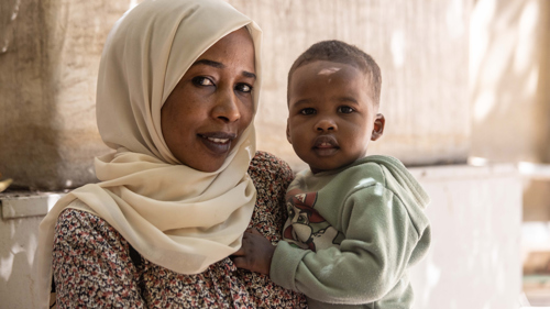 En kvinna håller sitt barn i famnen och tittar in i kameran.