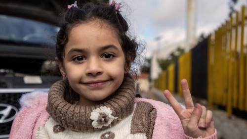 En flicka tittar in i kameran och gör fredstecken.