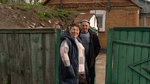 Ett ukrainskt par står framför en grön grind.