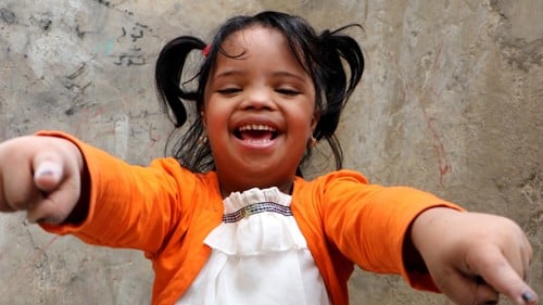 En glad flickar i orangea tröja tittar in i kameran.