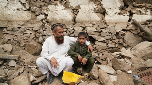 En pappa och son sitter bland stenar efter en jordbävning i Afghanistan 2025.
