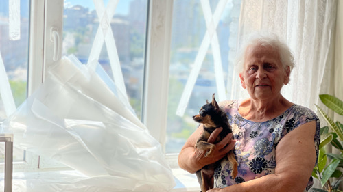En äldre kvinna håller sin hund i famnen och tittar mot kameran.