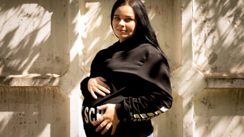 En gravid ukrainsk kvinna tittar mot kameran och håller sig varsamt om magen.