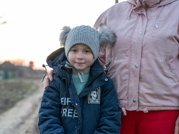 En familj i Ukraina står på en väg med sönderbombade hur.