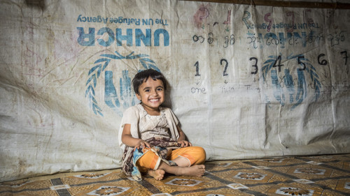 En liten flicka sitter i tält och skrattar.