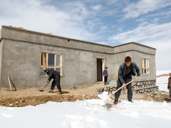 En familj röjer snö framför sitt nya hus i en bergsby i Afghanistan.