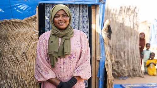 En kvinna sitter framför sitt hus. Hon ler mot kameran.