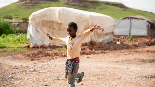 En pojke står på ett ben i ett flyktingläger. Han håller kursen.