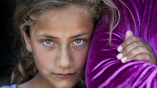 En flicka tittar in i kameran och kramar en annan persons arm.