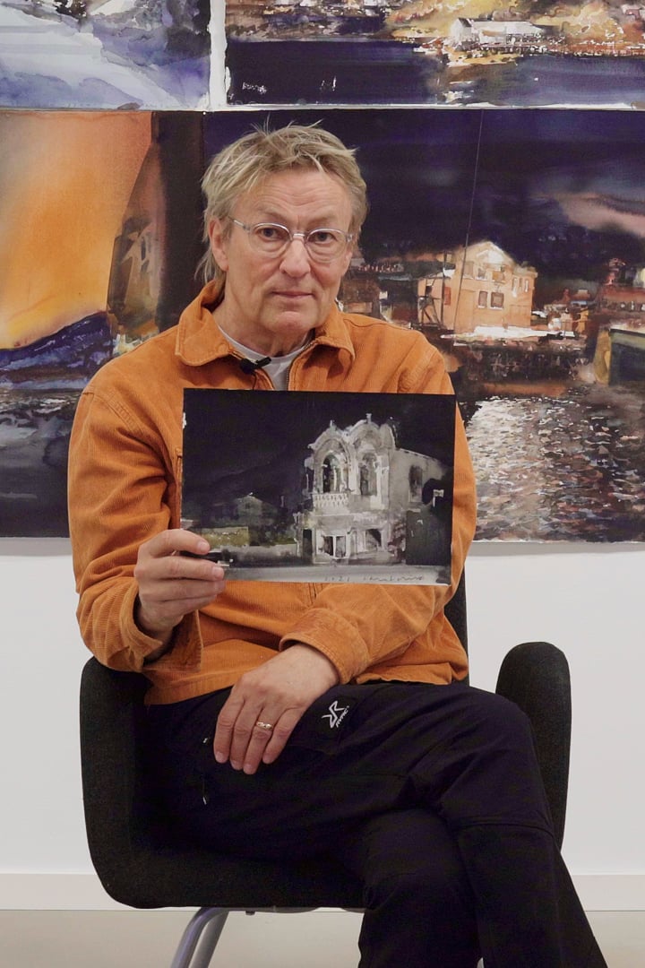 Lars Lerin sitter på en stol och håller upp en tavla.