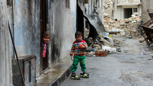 En liten pojke står i ruinerna i Syrien.