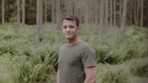 En man i grön tröja står i en skog.