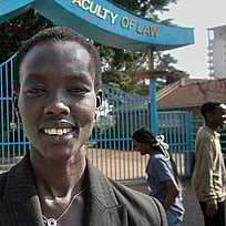 En kvinna står framför ingången till ett universitet. Hon ler mot kameran.