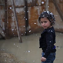 En liten flicka står utan vinterkläder i snö.