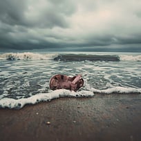 En sandal har spolats upp på en strand med vågor i bakgrunden.