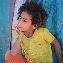 Ett litet barn på flykt sitter på madrasser i Jemen.