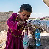 En pojke fyller på vatten från en vattenkran.