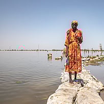 En kvinna står mellan två översvämmade fält i Sydsudan.