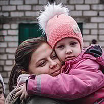 En mamma och dotter kramas och tittar in i kameran.