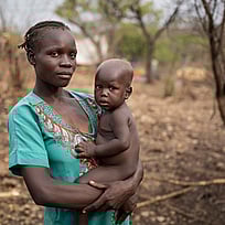 En kvinna håller sitt lilla barn i famnen. De tittar in i kameran.