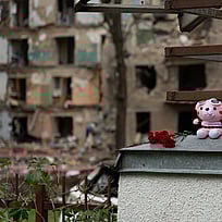Ett gosedjur är placerad på en mur med sönderbombade hem i bakgrunden.