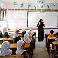 En kvinnlig lärare pratar till sina elever, som sitter i sina skolbänkar.