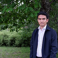 En ung man står framför en stor grönskande buske.