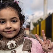 En flicka tittar in i kameran och gör fredstecken.