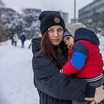 En familj står utanför sitt upplysta tält i ett flyktingläger.