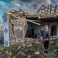 En kvinna tittar in i kameran. Hon står i rasmassorna från sitt eget hus i Ukraina.