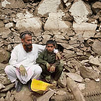 En pappa och son sitter bland stenar efter en jordbävning i Afghanistan 2025.