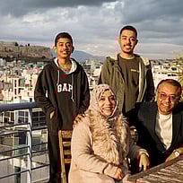 En familj med fyra personer tittar in i kameran och ler. I bakgrunden syns greklands huvudstad Aten.