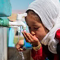 En flicka dricker vatten från en kran vid en renoverad skola i Afghanistan.
