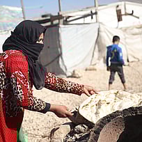 En kvinna i ett flyktingläger lagar bröd över en eld.